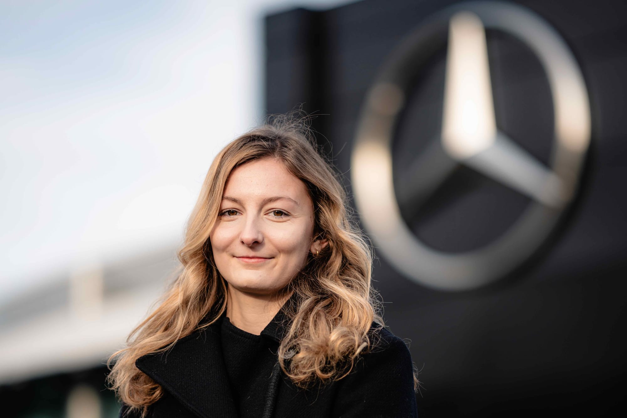 F1 Academy driver Doriane Pine stands in front of a Mercedes logo, 2024